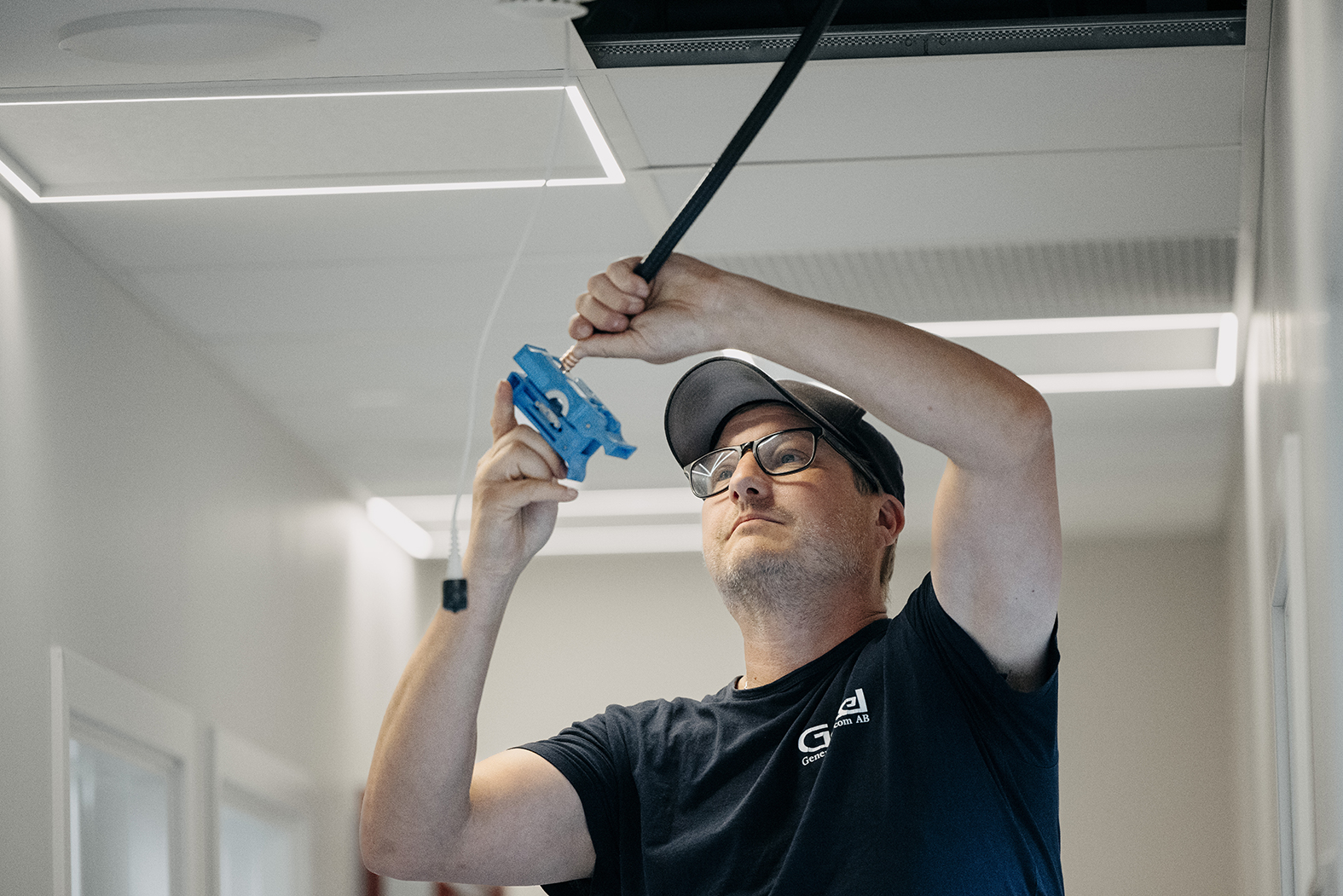 Tekniker drar kablar i ett undertak i en ljus kontorskorridor