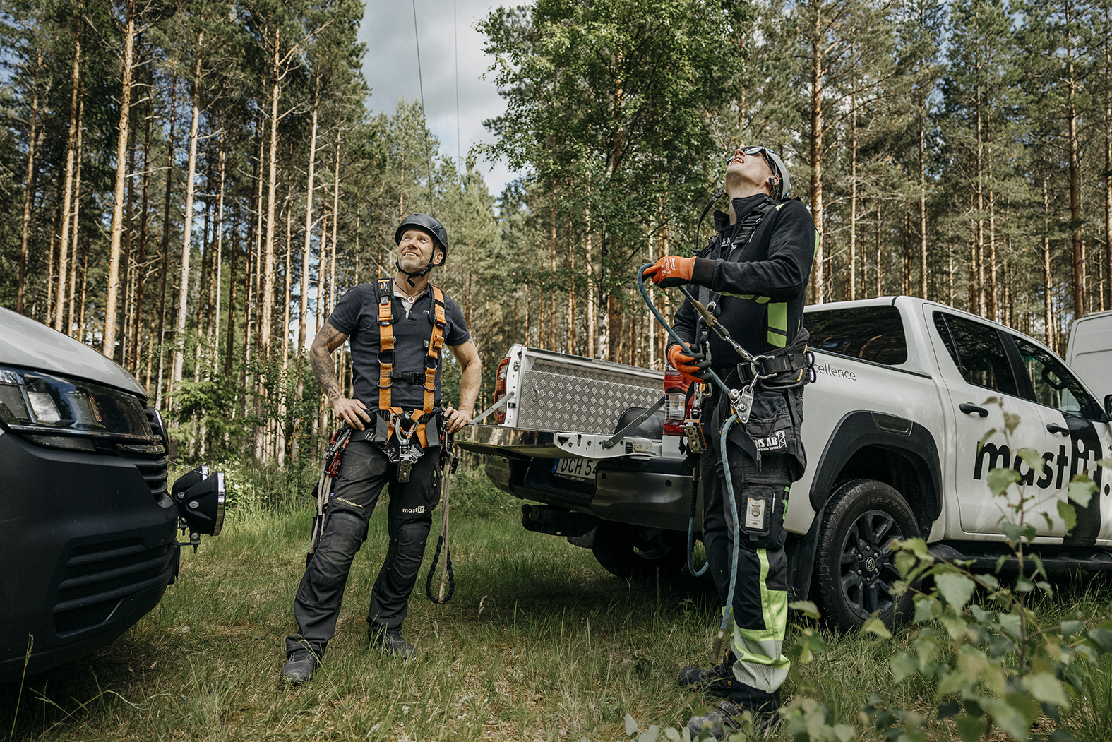 Två tekniker i klätterutrustning förbereder arbete vid en mast i skogen bredvid en servicebil